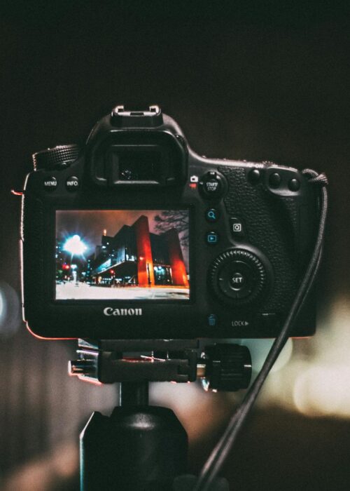 selective focus photography of black canon camera displaying photo of red and black building